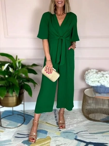 Detail of dark green V-neck jumpsuit with waist tie and side pockets in a studio setting