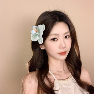 Close-up of elegant white orchid hair clip with pearl center on woman's wavy hair