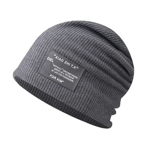 Detail view of a grey ribbed slouchy beanie featuring a black lettered fabric patch.
