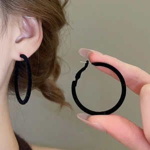 Macro shot of black flocked round earrings showing matte texture and minimalist geometric design