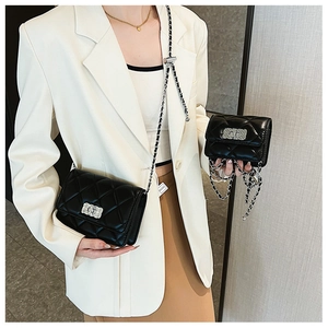 Close-up of black quilted small square bag with silver chain and metal buckle detail