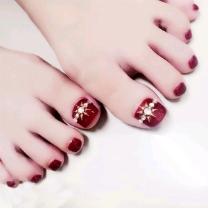 Close-up of burgundy press-on toenails featuring golden stars and rhinestone details