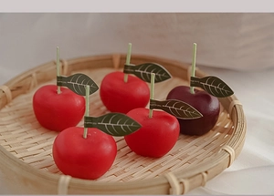 Primer plano de velas con forma de manzana roja y púrpura en bandeja de bambú tejida