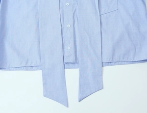 Close-up of light blue shirt hem featuring elegant button closure and decorative bow tie detail