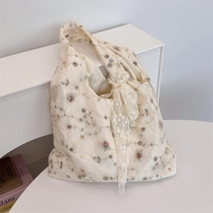 Close-up of floral embroidery detail and lace bow on ivory canvas tote shoulder bag