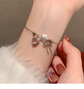 Detail of silver bangle featuring pink heart zircon, star and bow charms on model wrist