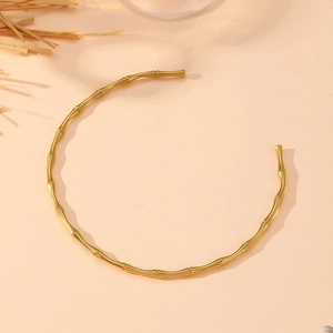 Detail of a minimalist gold bamboo choker necklace on a natural aesthetic background