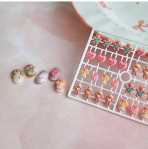 Macro shot of 3D bear and love heart resin nail art charms on a decorative white plate