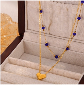 Detail of gold heart pendant necklace with blue beads in a beige jewelry box display
