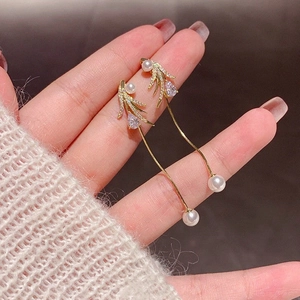 Close-up of golden tassel earrings with pearls, leaf charms and teardrop zircons