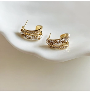 Macro shot of 14k gold-plated C-shaped earrings with layered pearls and cubic zirconia
