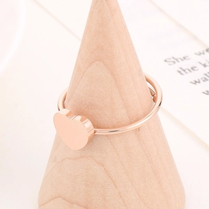 Detail of minimalist rose gold heart ring displayed on a wooden stand with soft lighting