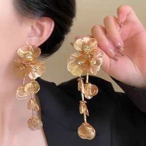 Detailed close-up of long gold flower tassel earrings with sparkling rhinestones on model