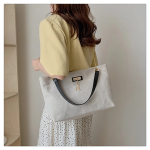 Detail of canvas tote bag with leather strap and golden deer pendant on a model