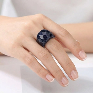 Macro view of a faceted navy blue sandstone ring with 18K gold plating on a model