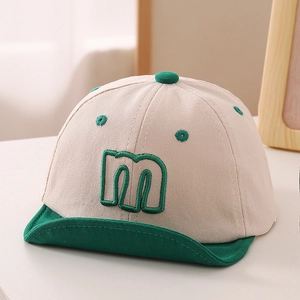 Detail of baby cotton cap with green embroidered letter M and soft brim design