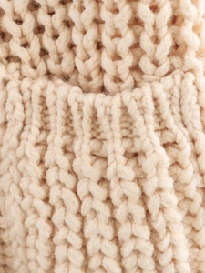 Macro view of beige thick knit fabric showing detailed texture and knitting craft