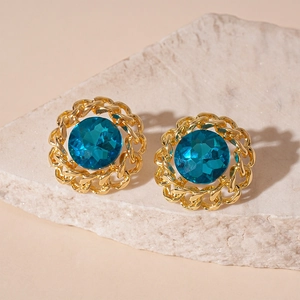 Detail of vintage gold chain earrings with blue gemstone on textured light stone base