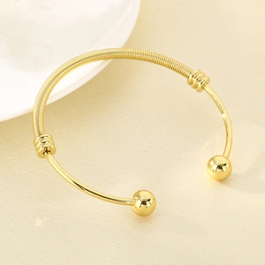 Detail of 18K gold plated mesh spring bracelet featuring round beads on a beige texture