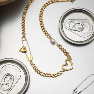 Detail of a gold Cuban link necklace with heart charms and a pearl on a metal surface