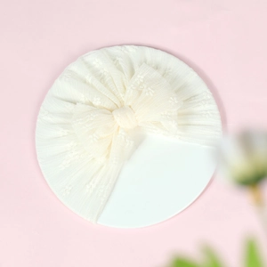 Close-up of cream lace baby turban featuring a large decorative bow and floral mesh detail