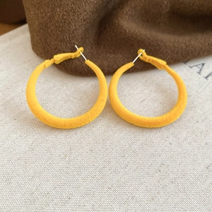 Détail de la boucle d'oreille créole floquée jaune avec texture velours sur tissu lin