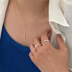 Close-up of minimalist silver water drop necklace and pearl rings on a model