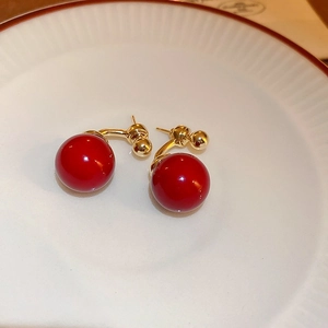 Detail of red bead earrings with golden metal link displayed on a white textured plate