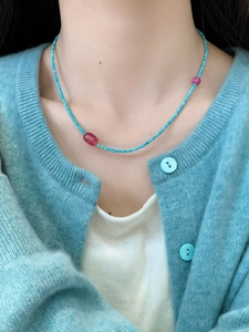 Close-up of beaded necklace with turquoise blue beads and red stones on a model