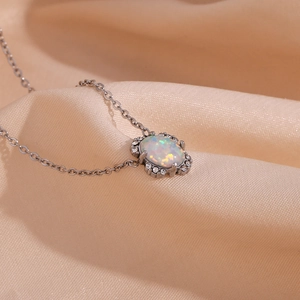 Elegante Silberkette mit ovalem Opal-Anhänger und Kristallen auf weichem Seidenstoff