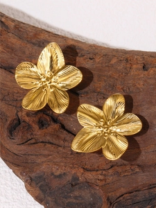 Detailed close-up of golden stainless steel flower earrings on a rustic wood background