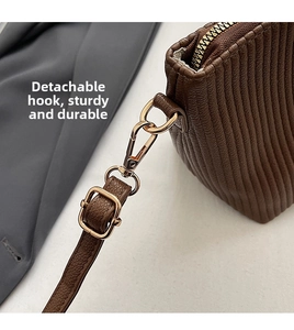 Detail of detachable golden hook and adjustable leather strap on brown pleated bag