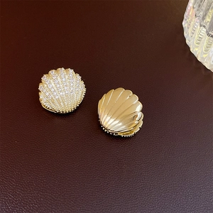 Asymmetric shell-shaped gold earrings with micro-set zircons on dark leather texture