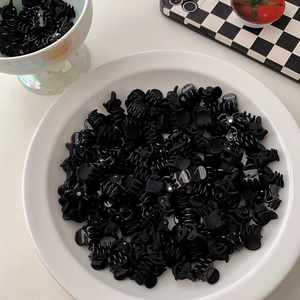 Close-up of bulk glossy black mini claw clips stacked in a white display plate