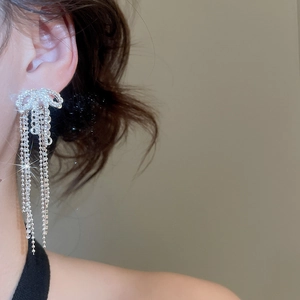 Macro shot of silver bow tassel earrings with sparkling rhinestones worn on a model's ear