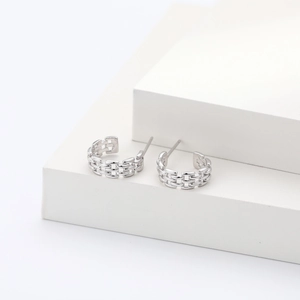 Detail shot of silver braided hoop earrings showcasing metallic texture on a white stand