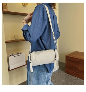 Detailed shot of white quilted cylinder bag with adjustable strap and diamond stitching