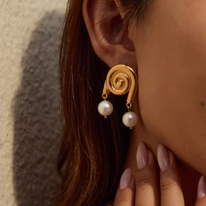 Close-up of elegant gold spiral earrings with white pearl drops worn by a model