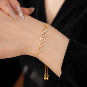 Détail du bracelet coeur doré avec zircons sur poignet contre fond en velours noir