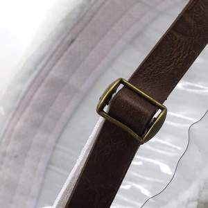 Detail of adjustable brown leather strap with antique brass buckle on the beanie hat
