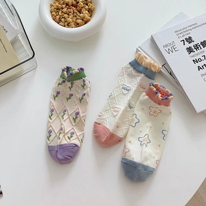 Three pairs of purple floral and heart pattern cotton socks with ruffle edges on a desk