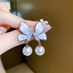 Close-up of butterfly pearl earrings with sparkling crystals held by hand