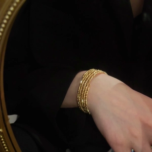 Detail of five-layer gold plated beaded cuff bracelet worn with elegant black blazer
