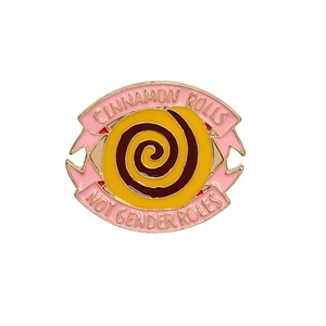 Detail of pink and yellow enamel pin with Cinnamon Rolls Not Gender Roles quote