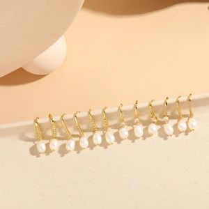Close-up of gold hoop earrings with hanging white pearls and zircon inlay detail