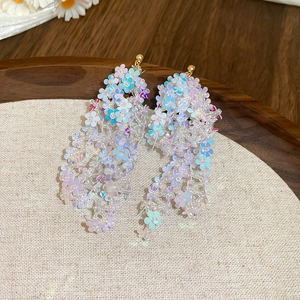 Detail of iridescent beaded flower tassel earrings on a wooden tray with a linen pad