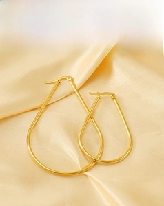 Macro shot of minimalist gold teardrop hoop earrings on a silk satin background