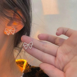 Detailed close-up of bow knot pearl earrings with micro-set pearls in warm light