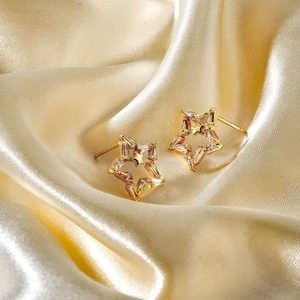 Boucles d'oreilles étoiles évidées dorées avec zircons sur un tissu en soie champagne