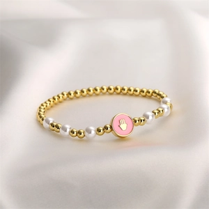 Détail macro du bracelet à billes dorées avec perles blanches et breloque main émaillée rose